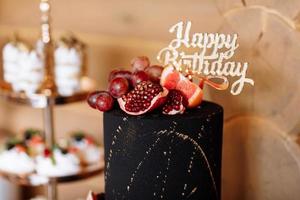 grote zwarte verjaardagstaart met vers fruit en snoep op een feestelijke tafel. snoepreep. tafel met verschillende snoepjes voor feest foto