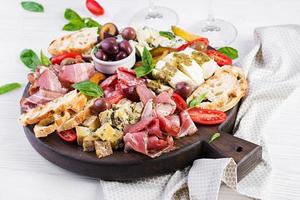 antipasto schotel met ham, prosciutto, salami, blauw kaas, Mozzarella met pesto en olijven Aan een houten achtergrond. foto