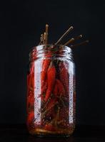 glas pot met gepekeld Chili paprika's Aan zwart achtergrond foto