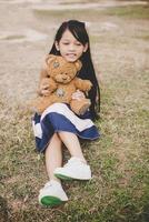 schattig Aziatisch meisje met teddybeer zittend in een veld