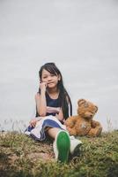 schattig Aziatisch meisje met teddybeer zittend in een veld foto