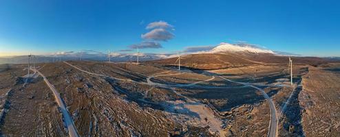 windmolens Aan de heuvels gedurende zonsondergang. hernieuwbaar energie, groen energie. bergen in de achtergrond met sneeuw. wind macht en milieuvriendelijk vriendelijk. duurzame toekomst. einde fossiel brandstoffen. foto