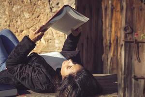 Latijns vrouw aan het liegen omlaag, lezing een boek in de tuin foto