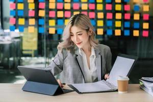 vrouw freelancer is werken haar baan Aan computer tablet en laptop aan het doen accounting analyse verslag doen van echt landgoed investering gegevens, financieel Bij kantoor foto