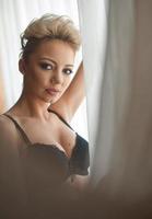 aantrekkelijk eerlijk haar- model- met panty en zwart beha en lang handschoenen poseren provocerend. mode portret van sensueel blond, studio schot. sensueel vrouw in zwart lingerie poseren tegen venster foto