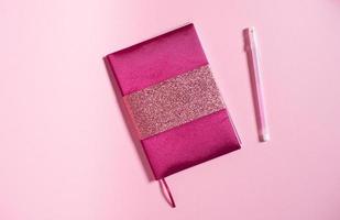 een roze notitieboekje met een glimmend decor leugens De volgende naar een pen Aan een roze achtergrond foto
