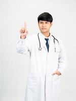 Aziatisch Mens leerling wetenschapper of dokter een persoon, vervelend een wit gewaad, staan, op zoek en lachend, wit achtergrond met een stethoscoop ausculteren de hart in de omgeving van zijn nek. foto