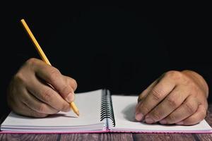 twee handen met geel potlood dat op notitieboekje schrijft