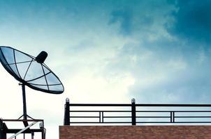 zwart satelliet schotel of TV antennes Aan de gebouw met de blauw lucht bewolkt achtergrond. foto