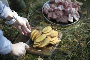 Koken voedsel in natuur. handen snijdend aardappelen voor barbecue. picknick. foto