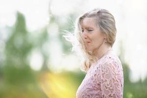 mooi ouderen vrouw met lang vloeiende haar. een vrouw geniet natuur en wind. romantisch portret van een mooi ouderen vrouw. volwassen mooi blond in een roze jurk. foto