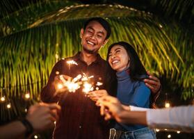 portret van gelukkig Aziatisch groep van vrienden hebben pret met sterretjes buitenshuis - jong mensen hebben pret met vuurwerk Bij nacht tijd - mensen, voedsel, drinken levensstijl, nieuw jaar viering concept. foto