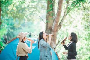 jong Dames juichen en drinken drank voorkant van camping tent foto