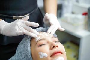 detailopname en Bijsnijden schoonheid vrouw maken gezicht spa en gelaats masker van room naar staat en traktatie de gezicht in schoonheid kliniek. foto