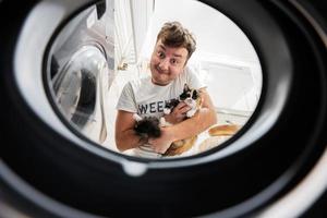 Mens met kat visie van het wassen machine binnen. mannetje doet wasserij dagelijks routine. foto
