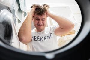 Mens visie van het wassen machine binnen. mannetje doet wasserij dagelijks routine. van streek, tranen de haar- Aan zijn hoofd. foto