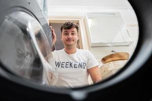 Mens visie van het wassen machine binnen. mannetje doet wasserij dagelijks routine. foto