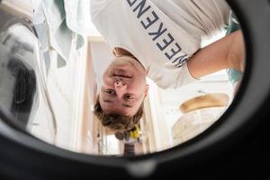 Mens visie van het wassen machine binnen. mannetje doet wasserij dagelijks routine. hoofd ondersteboven omlaag. foto