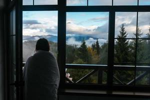 jong vrouw is op zoek door de venster Bij de bergen foto