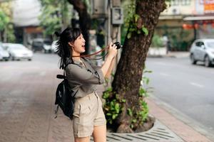 jong Aziatisch vrouw rugzak reiziger gebruik makend van digitaal compact camera, genieten van straat cultureel lokaal plaats en glimlach. reiziger controle uit kant straten. foto