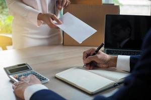 de bedrijf vrouw heeft een bruin karton doos De volgende naar haar lichaam en stuurt een brief van ontslag naar de leidinggevend. omvatten over ontslag, baan plaatsing en vacatures. foto