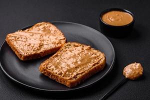 voedzaam belegd broodje bestaande van brood en pinda boter Aan een zwart keramisch bord foto