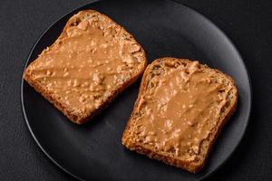 voedzaam belegd broodje bestaande van brood en pinda boter Aan een zwart keramisch bord foto