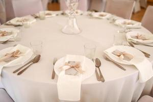 bruiloft tafel instelling met wit bord, bril en zilver bestek. mockup blanco met roze lint Aan bord foto