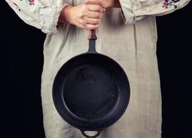 vrouw in een grijs linnen jurk houdt met twee handen een ronde gietijzer pan foto