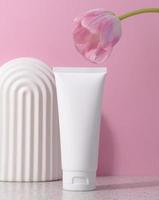 wit plastic buis voor kunstmatig producten Aan een roze achtergrond met een boog en een roze tulp, reclame en branding van producten foto