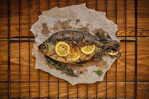 gebakken vis gekookt Aan perkament papier met kruiden, citroen en rozemarijn barbecue rooster met houten achtergrond. foto