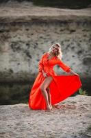 mooi vrouw in oranje jurk poseren Bij de achtergrond van zand heuvel foto