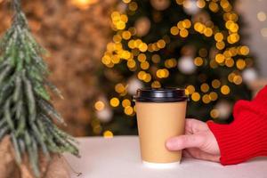 een beschikbaar kop naar zetten een hand- in een rood trui Aan de tafel in de buurt de Kerstmis boom foto