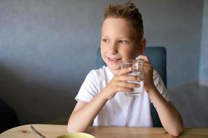 een schattig jongen drankjes water en eet een droog ontbijt Bij huis en glimlacht foto