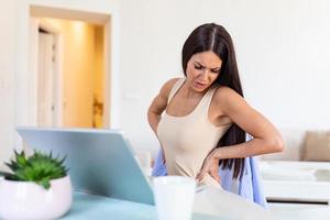 van streek jong vrouw voelt terug pijn masseren pijn doen spieren, verdrietig dame lijdt van lage rug lumbaal pijn zittend in niet correct sedentair houding, rugpijn radiculitis concept foto