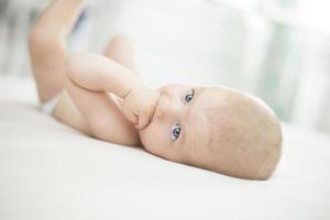 babymeisje liggend met hand in de mond foto