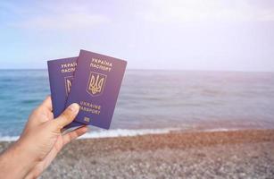 twee biometrisch oekraïens paspoorten in hand- Aan zee kust achtergrond foto