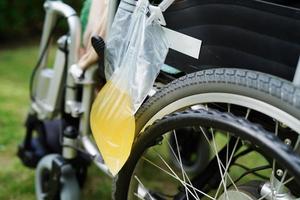 Aziatische handicap vrouw met urinezak op rolstoel. foto
