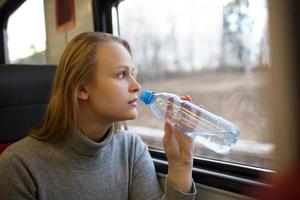 vrouw drinkwater en kijkt uit treinraam foto