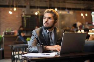 jonge zakenman kopje koffie houden tijdens het werken op laptopcomputer in coffeeshop