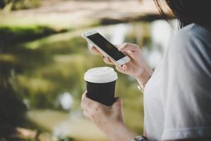 jonge vrouw met wegwerp koffiekopje terwijl tekstberichten via smartphone buitenshuis