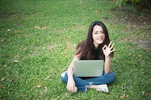 jonge mooie vrouw zittend op het groene gras en met behulp van laptop in het park foto