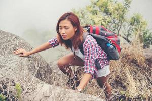 jonge Aziatische vrouwenwandelaar die rots op bergtop beklimt foto
