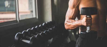 man met een halter in een sportschool met rij halters op de achtergrond foto