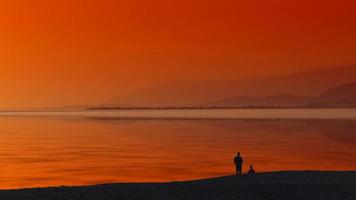 zeegezicht met oranje zonsondergang en silhouetten van mensen op het strand foto