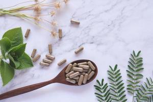 kruidengeneeskunde in capsules op houten lepel met natuurlijk groen blad op wit marmer foto