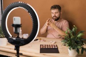 portret van gelukkig Mens schoonheid blogger zittend in kamer Bij tafel en sprekend aanbevelen fundament of decoratief kunstmatig op zoek Bij camera. bloggen en vlog concept foto