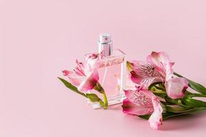 een chique fles van vrouwen parfum of toilet water Aan een roze achtergrond met delicaat astromerie bloemen. een kopiëren van de ruimte. aroma presentatie. foto