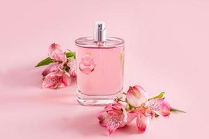 een chique fles van vrouwen parfum of toilet bloem water Aan een roze achtergrond tussen de bloemen van. roze achtergrond. modern bloemen geur. foto