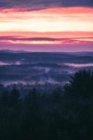 luchtfoto van landschap met bomen, heuvels, mist en bergen met kleurrijke bewolkte zonsopgang foto